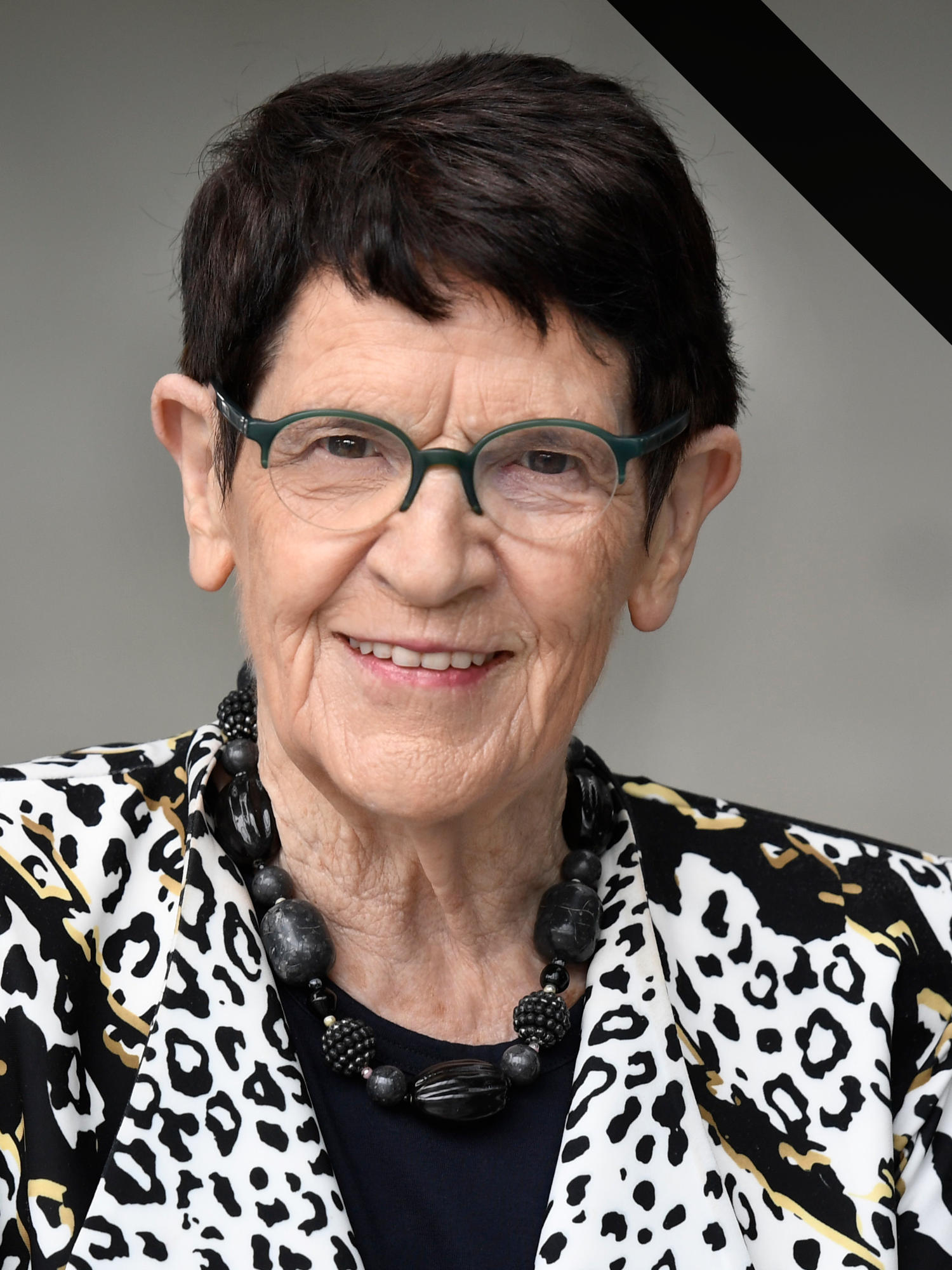 Rita Süssmuth vor neutralem Hintergrund. Sie schaut freundlich in die Kamera, trägt ein gemustertes Jackett. Das Bild ist oben rechts mit einer schwarzen Binde als Zeichen der Trauer versehen.